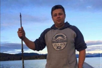 A man wearing an Alaska sweatshirt and holding a spear gun