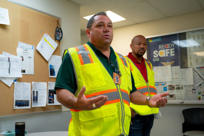 Two men in hi-visibility vests standing in front of a bulletin board