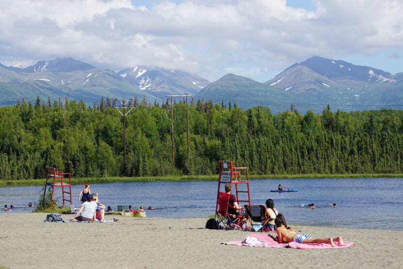 People lying on a beach at a lake with mountains in the background