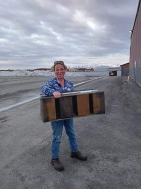 A standing by an airport hangar, holding a bee hive