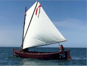 A small sailing boat with one man in the stern