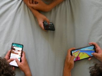three sets of hands holding smart phones on a sheet
