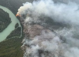 A wildfire burning by the bank of a river, seen from the air