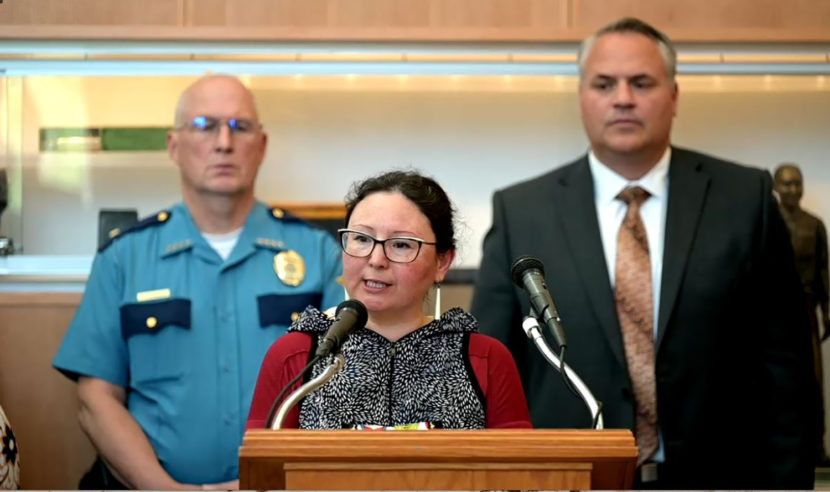 A woman at a lectern with two men standing behind her