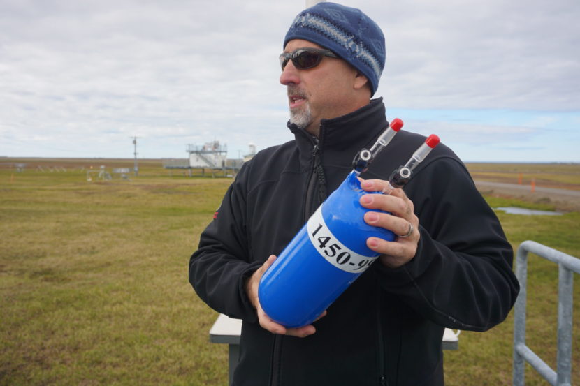 A man stands on the tundra holding a blue canister