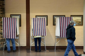 A man walks past three voting booths, two of them occupied