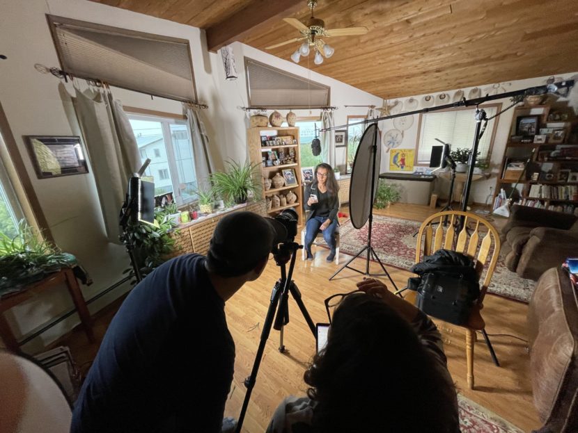 Mary Peltola sits on a chair in a living room with a reflector next to her and a cameraman filming