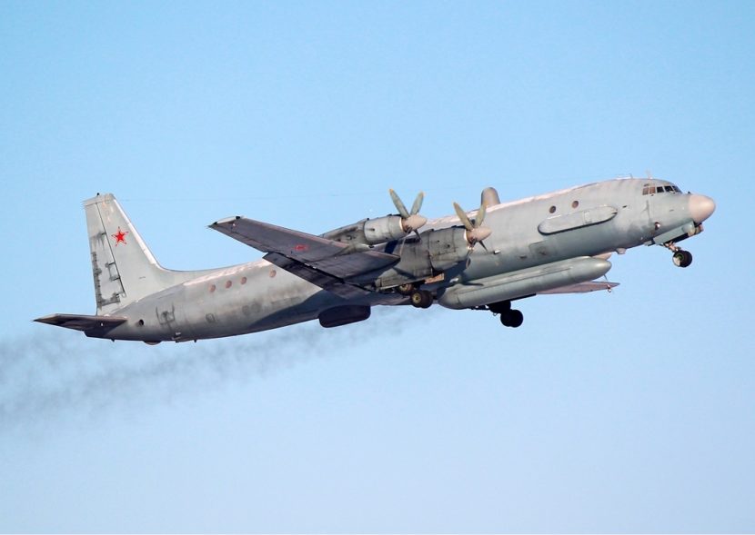 A four-propellor Russian military plane climbing and trailing black exhaust