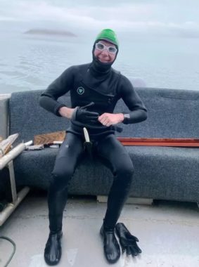 A smiling man in a wetsuit sitting in the stern of a boat