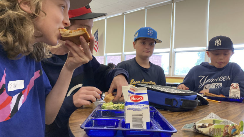 school kids eating pizza around a cafeteria table