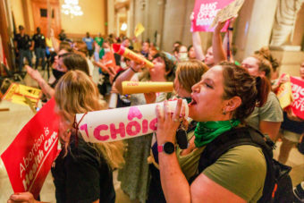 A large group of people shout and hold pro-choice signs inside a public building