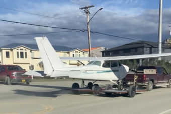 A small private plane being towed down a public street on a trailer