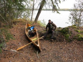 A man sits by a canoe pulled up on the bank