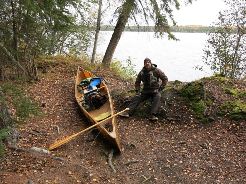 A man sits by a canoe pulled up on the bank