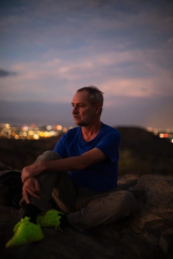 A man sits on a hill at night with a city below him