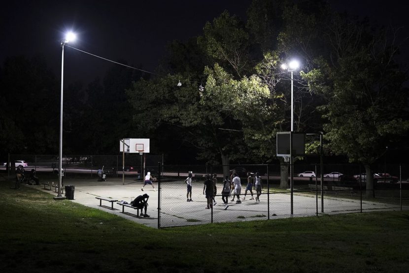 People on a lit basketball court in a park at night