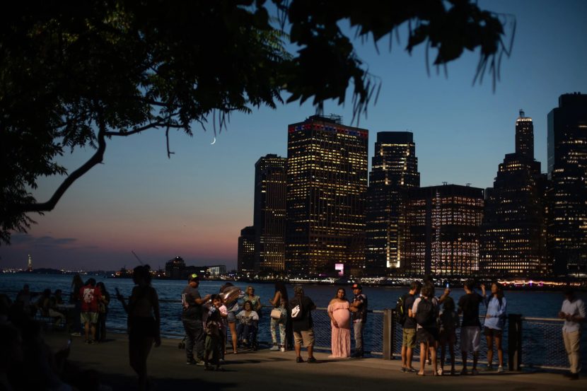 People on a river walk at night with the city skyline across the water behind them