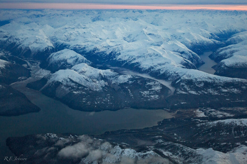 An aerial photo of a lake surrounded by snowy mountains