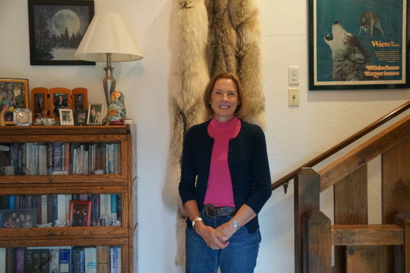 A woman stands in front of hanging wolf pelts and next to a framed poster of howling wolves