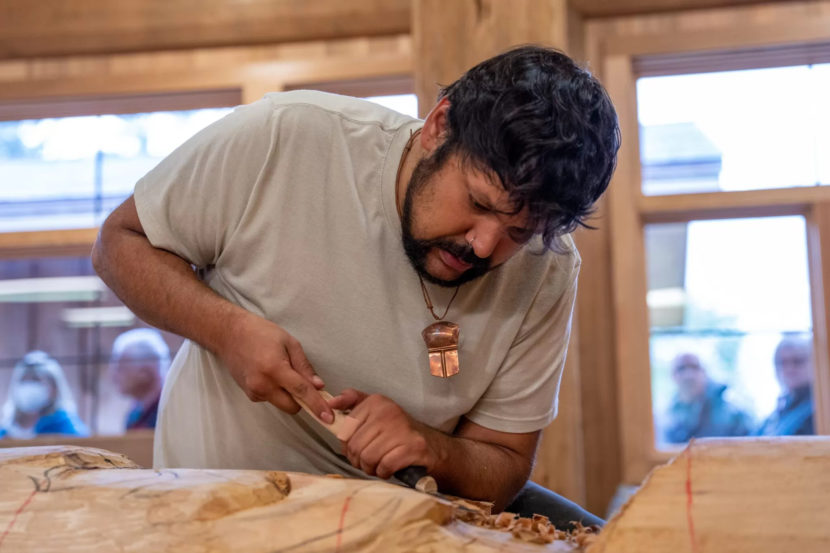 A man carving a pole with a chisel