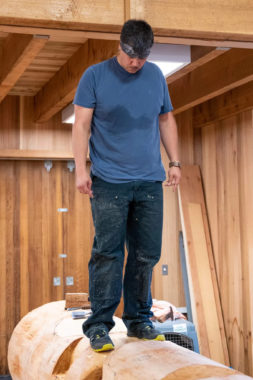 A sweaty man stands on top of a pole in progress in a woodshop