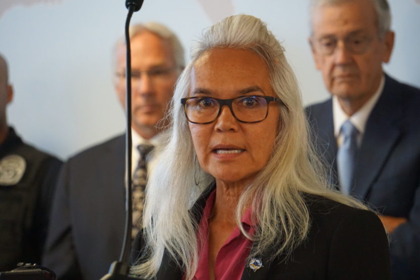 A woman speaks at a press conference with men in suits behind her
