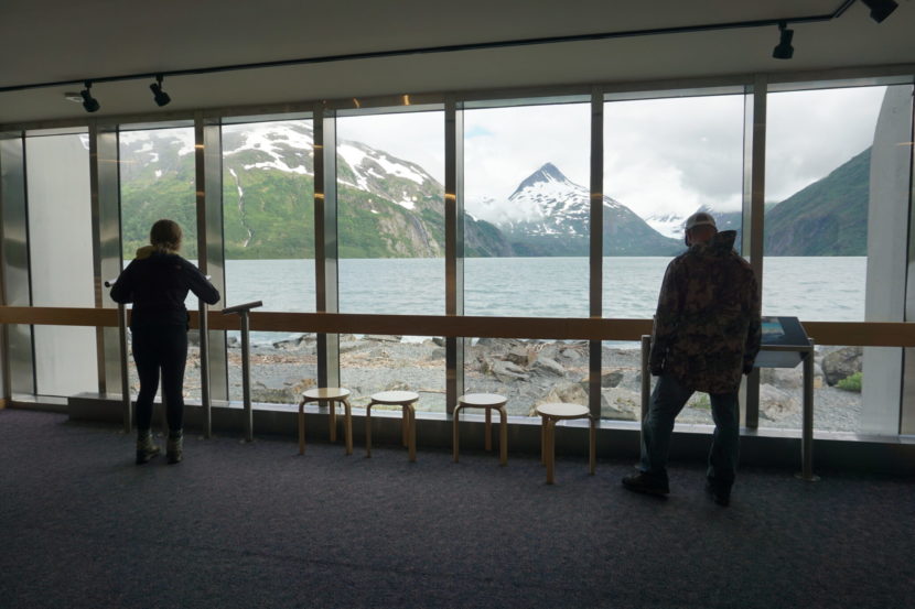People inside a visitors center standing by a wall of windows looking out on a lake.