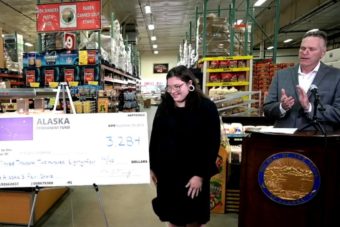 Gov. Dunleavy claps and looks at a woman who is standing next to a giant check