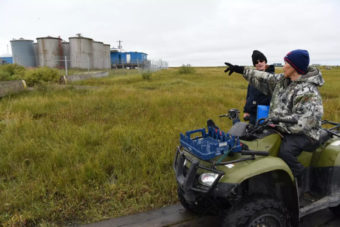 A person on an ATV points at a set of fuel tanks on the tundra