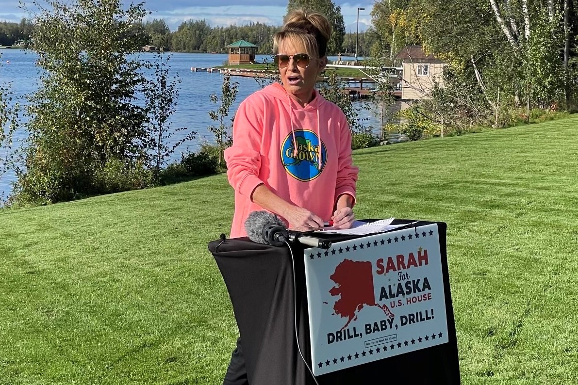 Sarah Palin stands at a podium in a pink Alaska Grown hoodie 