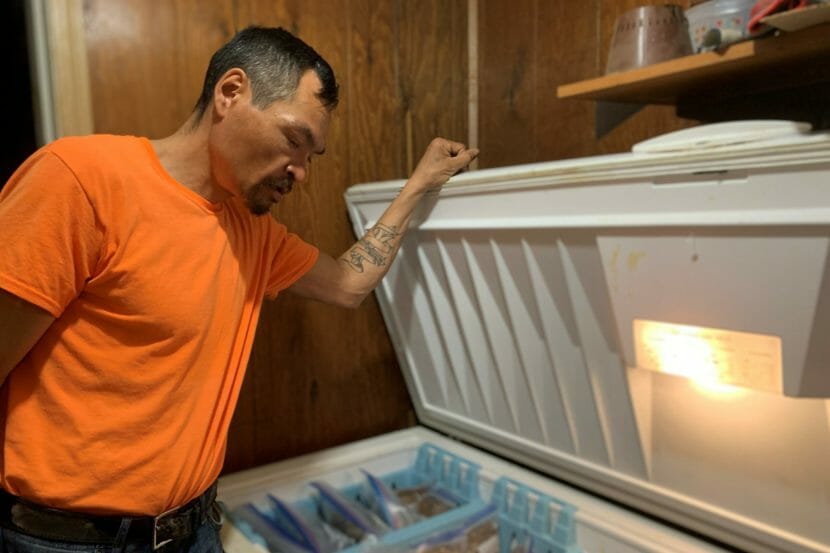 A man holds the lid up and looks into a large freezer