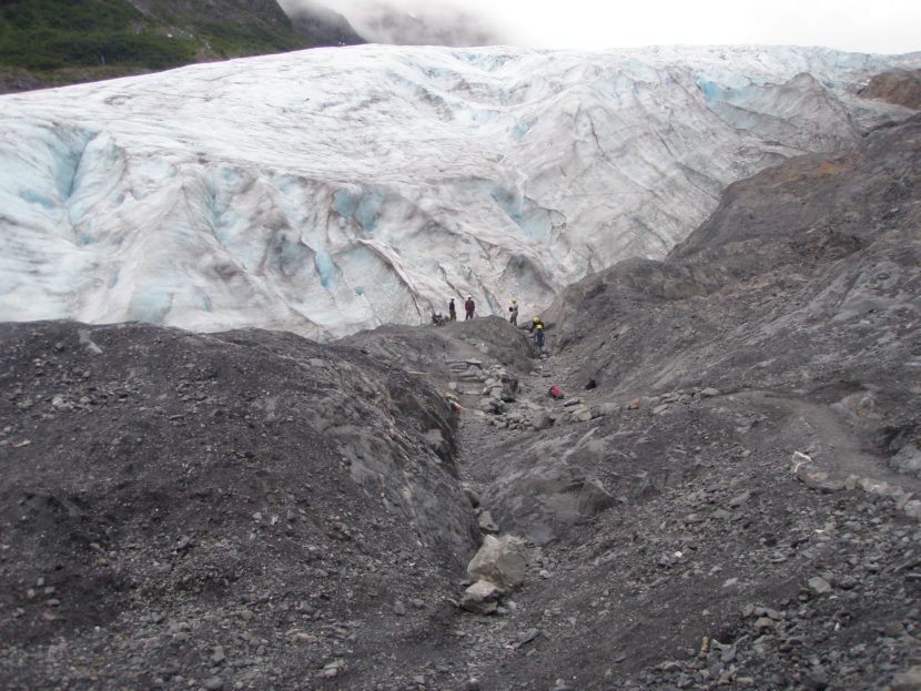 Seen from a distance, people working near the terminus of a glacier