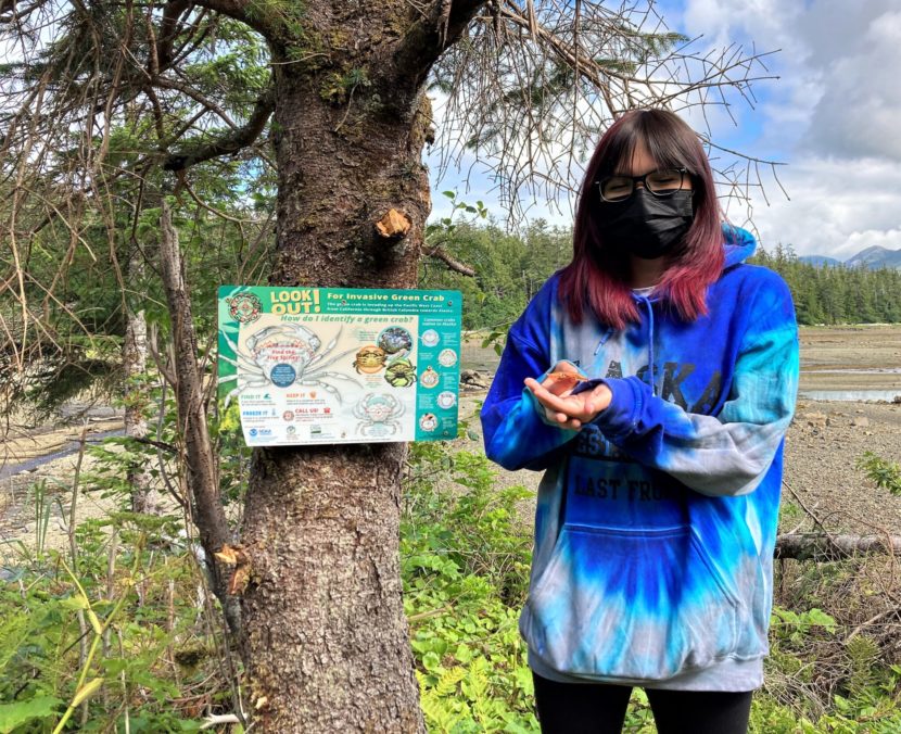 A woman stands by a tree holding a small crab shell