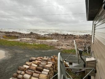 Seen from next to a house, wood and debris piled up at the edge of an angry sea