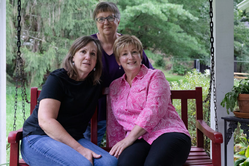 Three women post for a photo on and around a red porch swing
