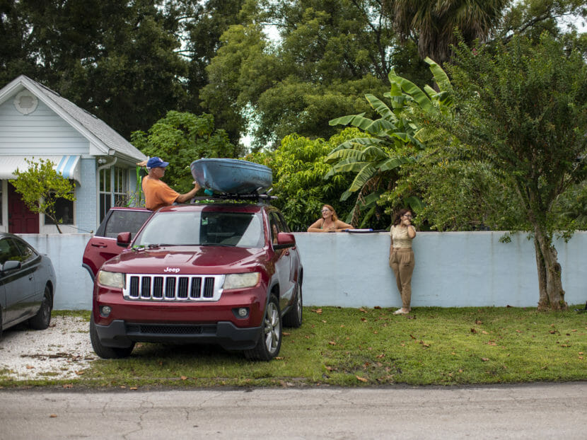 A man straps a boat to the top of an SUV while two women watch