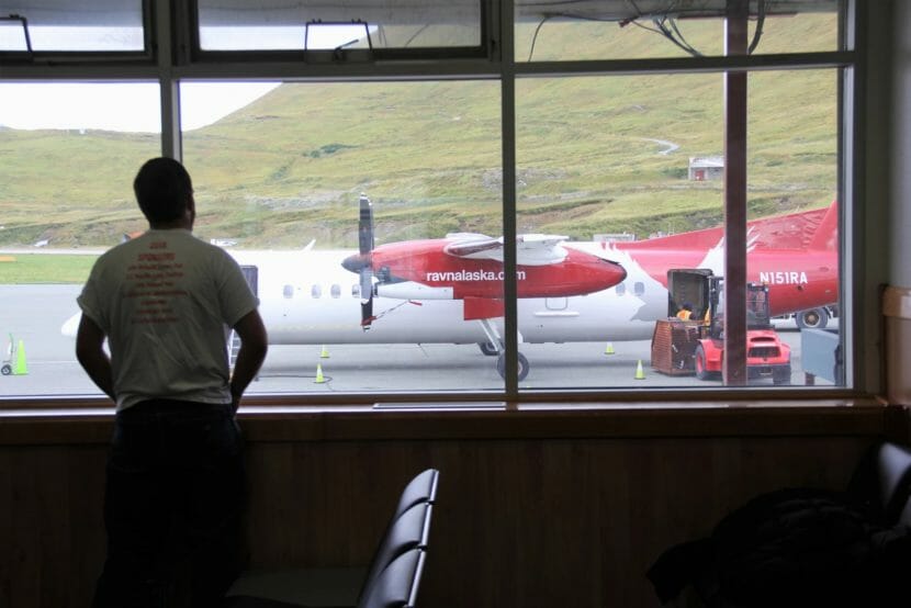 A man stands at a gate in Unalaska's airport looking out at a Ravn plane on the tarmac.