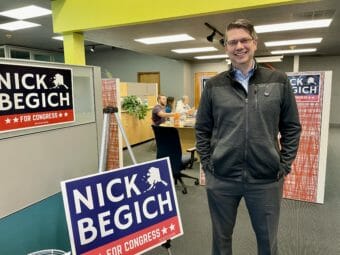 Nick Begich stands next to a Nick Begich sign inside a large office space.