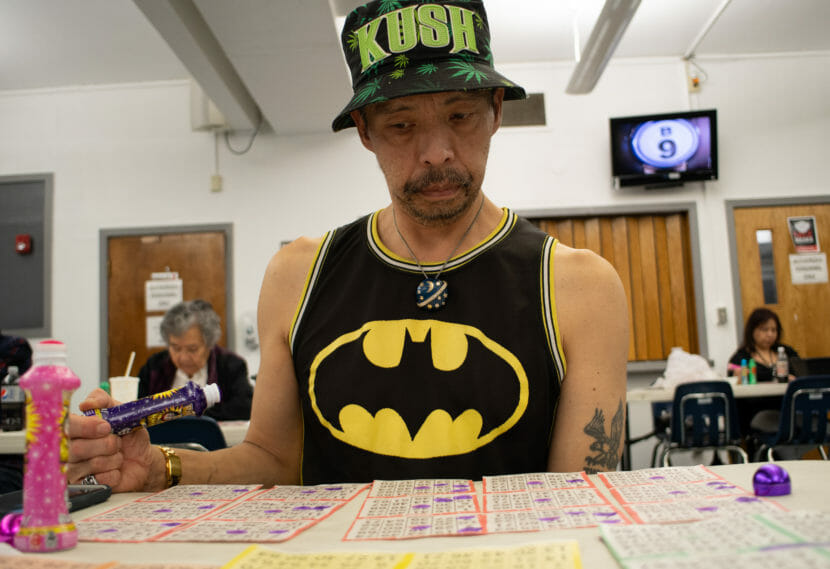 A man in a bucket hat and a batman tank top looks down at his bingo cards