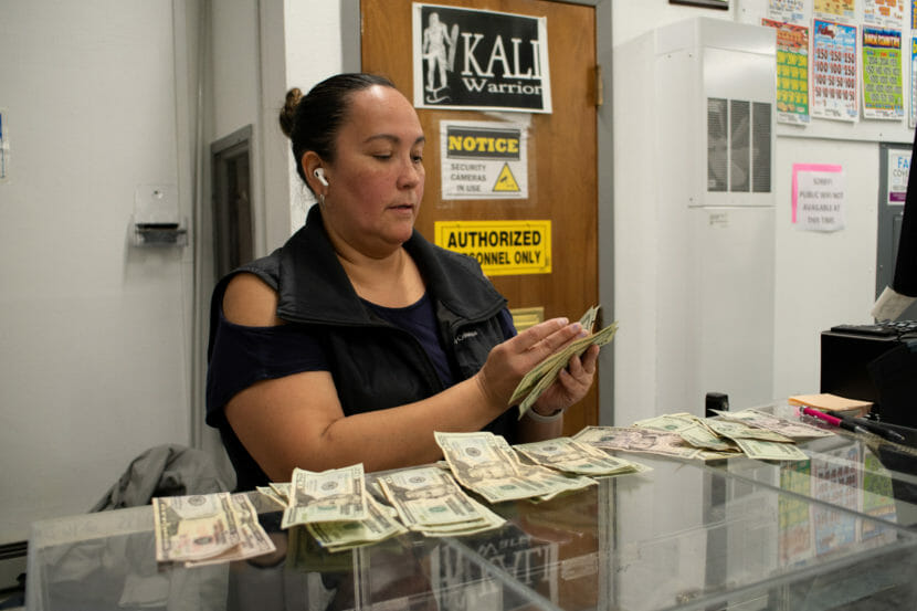 A woman counting money behind a glass counter. Several small stacks of bills are laid out on the counter in front of her.