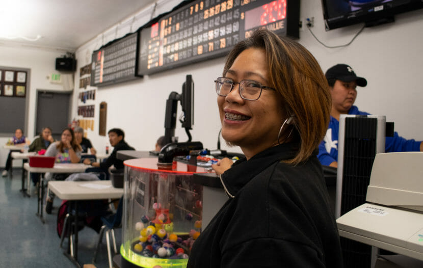 A woman looks back at the camera smiling as people play bingo behind her