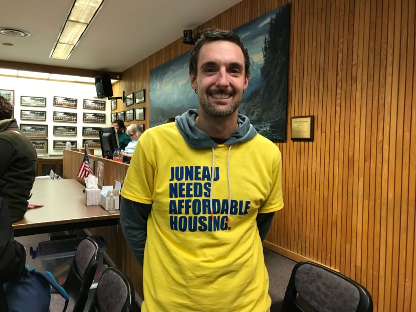 A man smiling and wearing a yellow shirt that says "Juneau needs affordable housing"