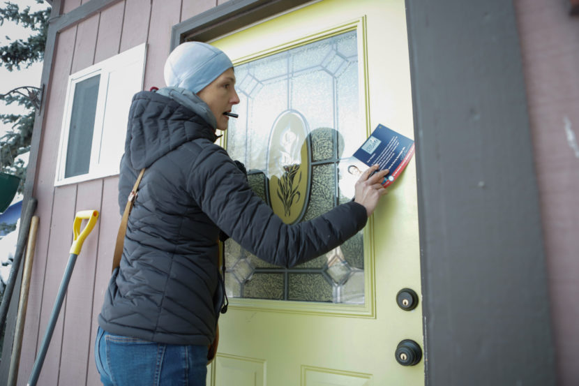 A woman holds a pen in her mouth while slipping a political flyer into the side of a door