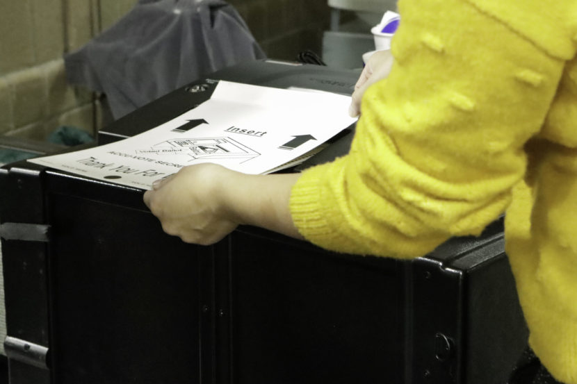 A person inserting a ballot in its privacy sleeve into a ballot box