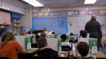 A view of students sitting at their desks, from the back of the classroom