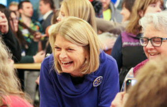 Murkowski, in a room full of people, leans forward and laughs