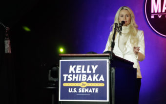 Kelly Tshibaka speaks from behind a lectern in front of a purple wall