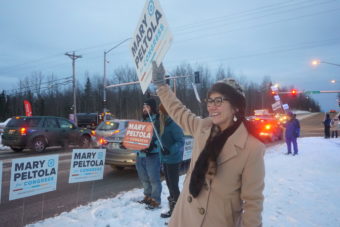 Mary Peltola and supporters wave signs by a city street in the snow