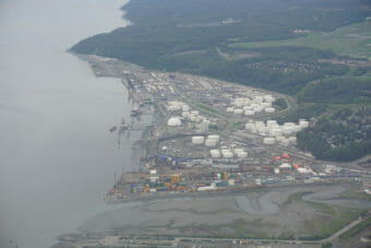An aerial photo of showing a coastal industrial area, with docks, many large tanks and stacks of shipping containers.