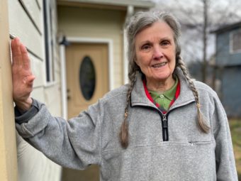 A portrait of an older woman standing outside a beige house